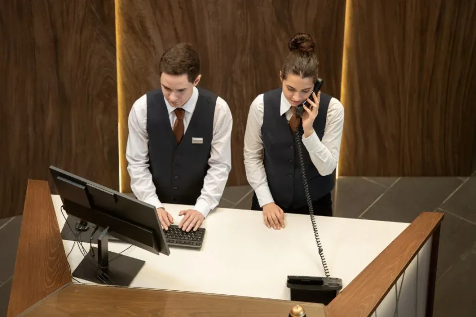 Hotel reception staff handling guest requests, phone calls, and computer-based tasks during daily operations.